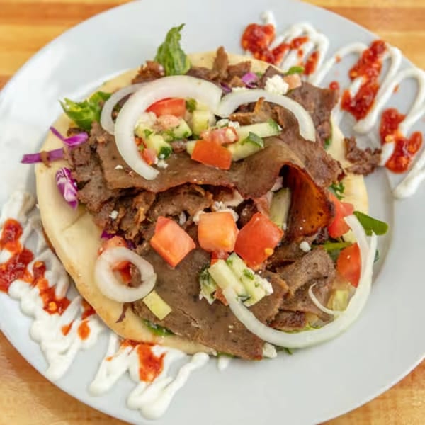 Sila's Mediterranean Restaurant's gyro with meat, onions, tomatoes, and sauce on a white plate.