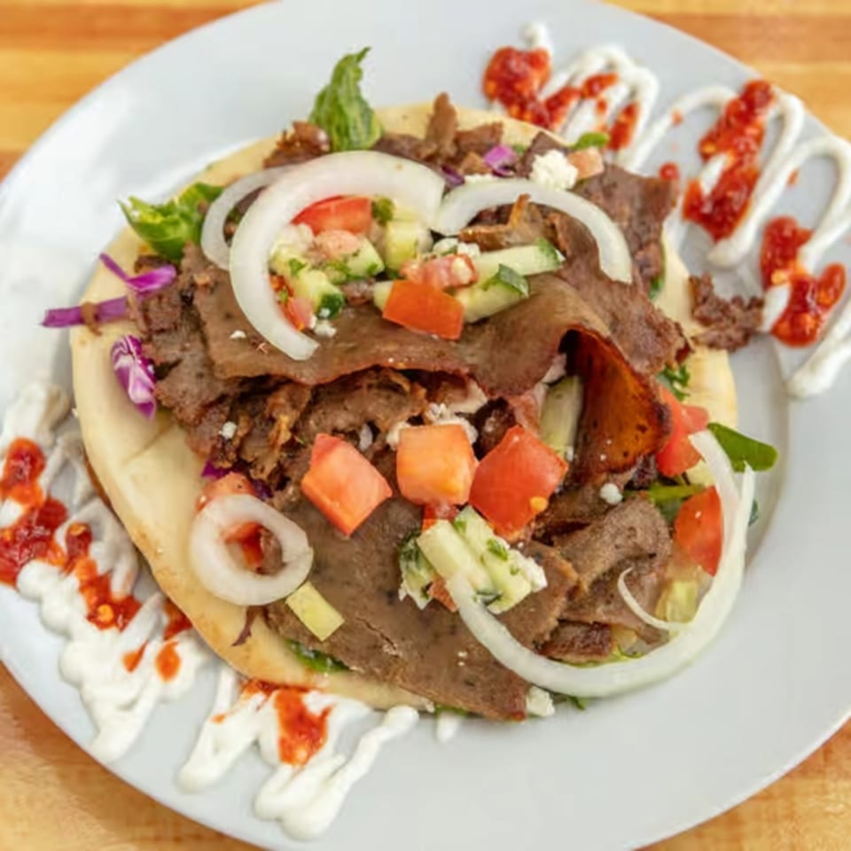 Sila's Mediterranean Restaurant's gyro with meat, onions, tomatoes, and sauce on a white plate.