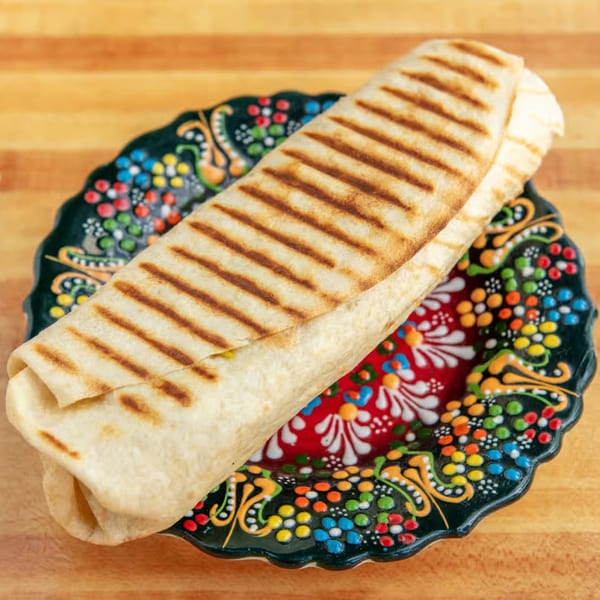 Grilled Mediterranean wrap on a colorful, patterned plate, resting on a wooden surface.