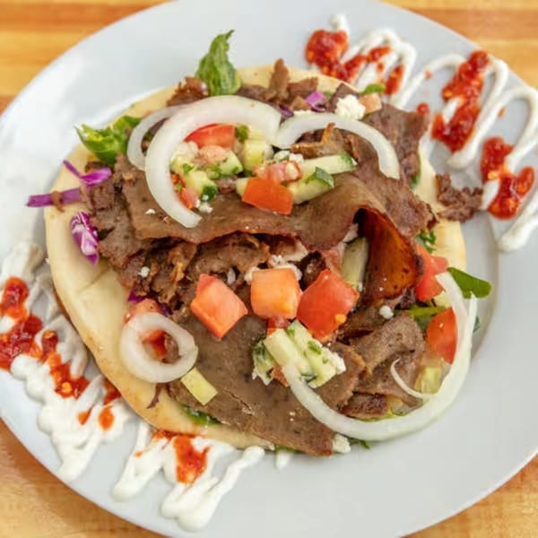 Sila's Mediterranean Restaurant's gyro with meat, onions, tomatoes, cucumbers, and sauces on a white plate.