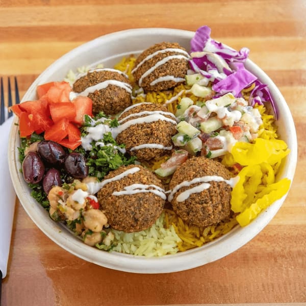 A Mediterranean falafel bowl with rice, tomatoes, olives, chickpeas, and pickled vegetables.