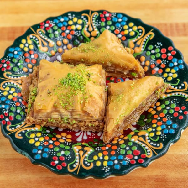 Three pieces of Sila's Mediterranean baklava, garnished with pistachios, on a colorful patterned plate.