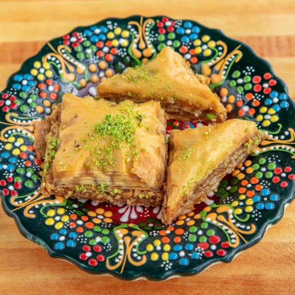 Three pieces of baklava, one square and two triangles, on a colorful, patterned plate.