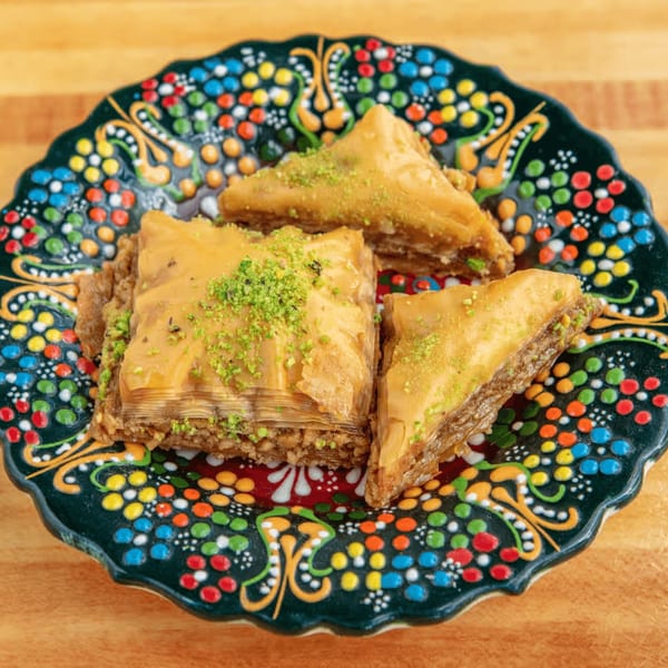 Three pieces of baklava, two triangular and one square, topped with pistachios on a colorful plate.