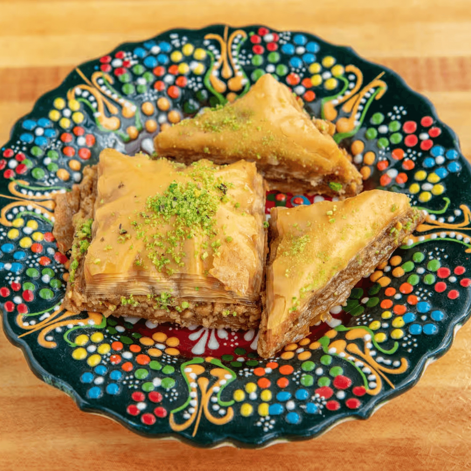Three pieces of baklava, two triangular and one square, topped with pistachios on a colorful plate.